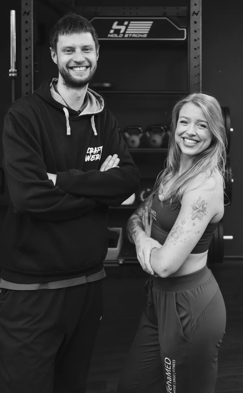 Die beiden Gesichter des Kraftwerks: Trainerin im rehaMED-Outfit und Trainer im Kraftwerk-Hoodie vor dem Rack
